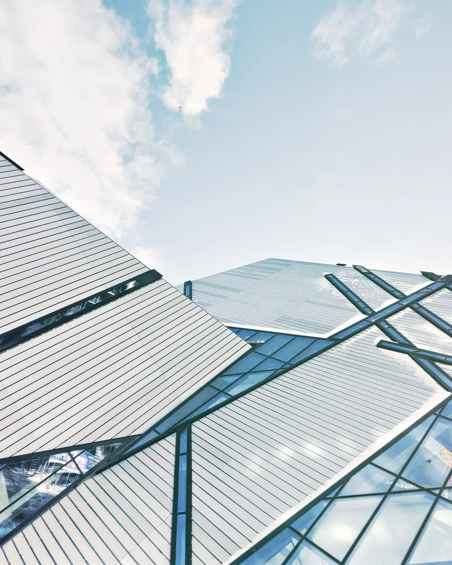 Looking up the glass and metal flank of a tower, two faces meeting at a ridge against an open sky
