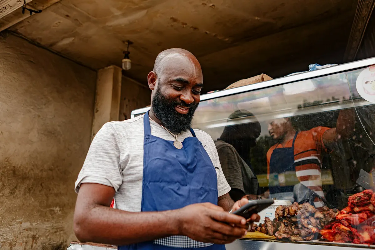 A butcher in a blue apron smiling at his phone behind the counter