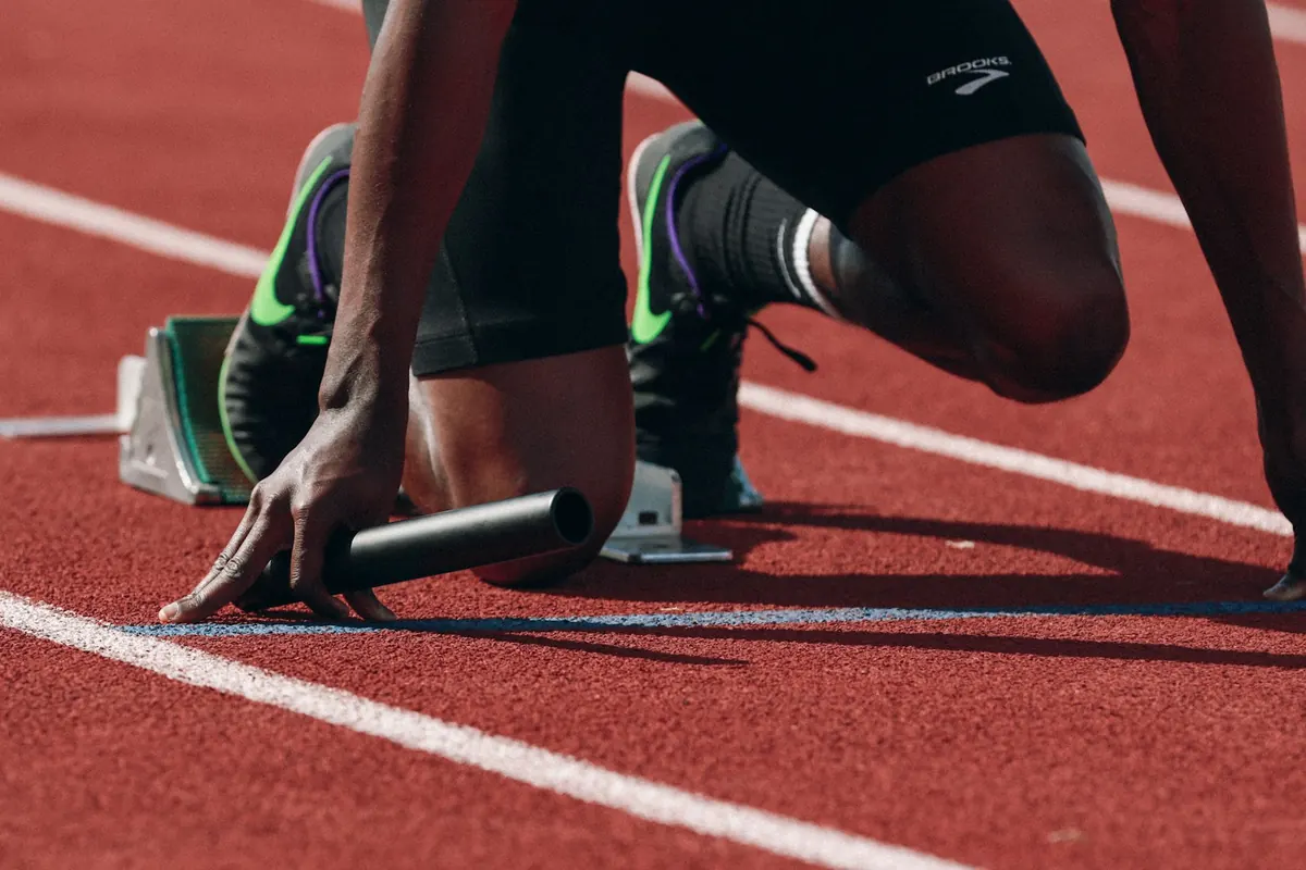 A sprinter crouched at the starting blocks holding a relay baton