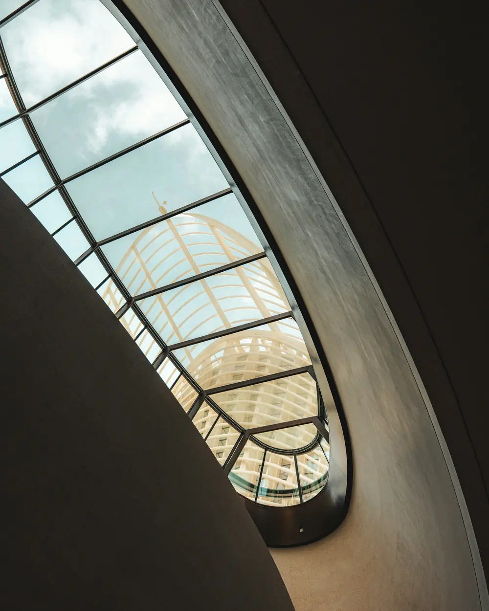 An oval skylight opening onto cloud, seen from inside a curved concrete shell