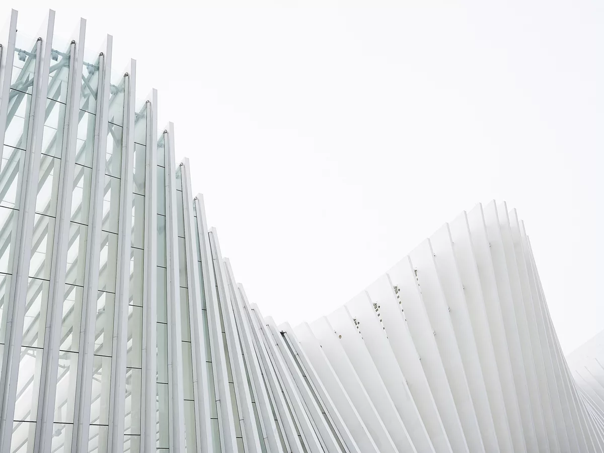 A white ribbed facade curving against an overcast sky, its structure fully visible