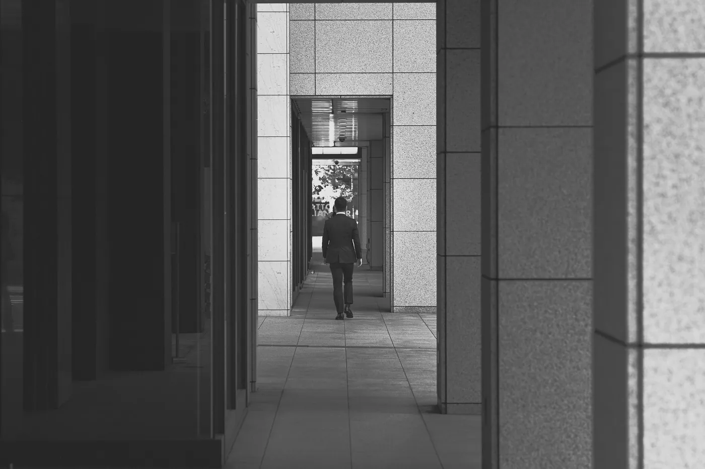 A figure walking away down a colonnade of square stone piers