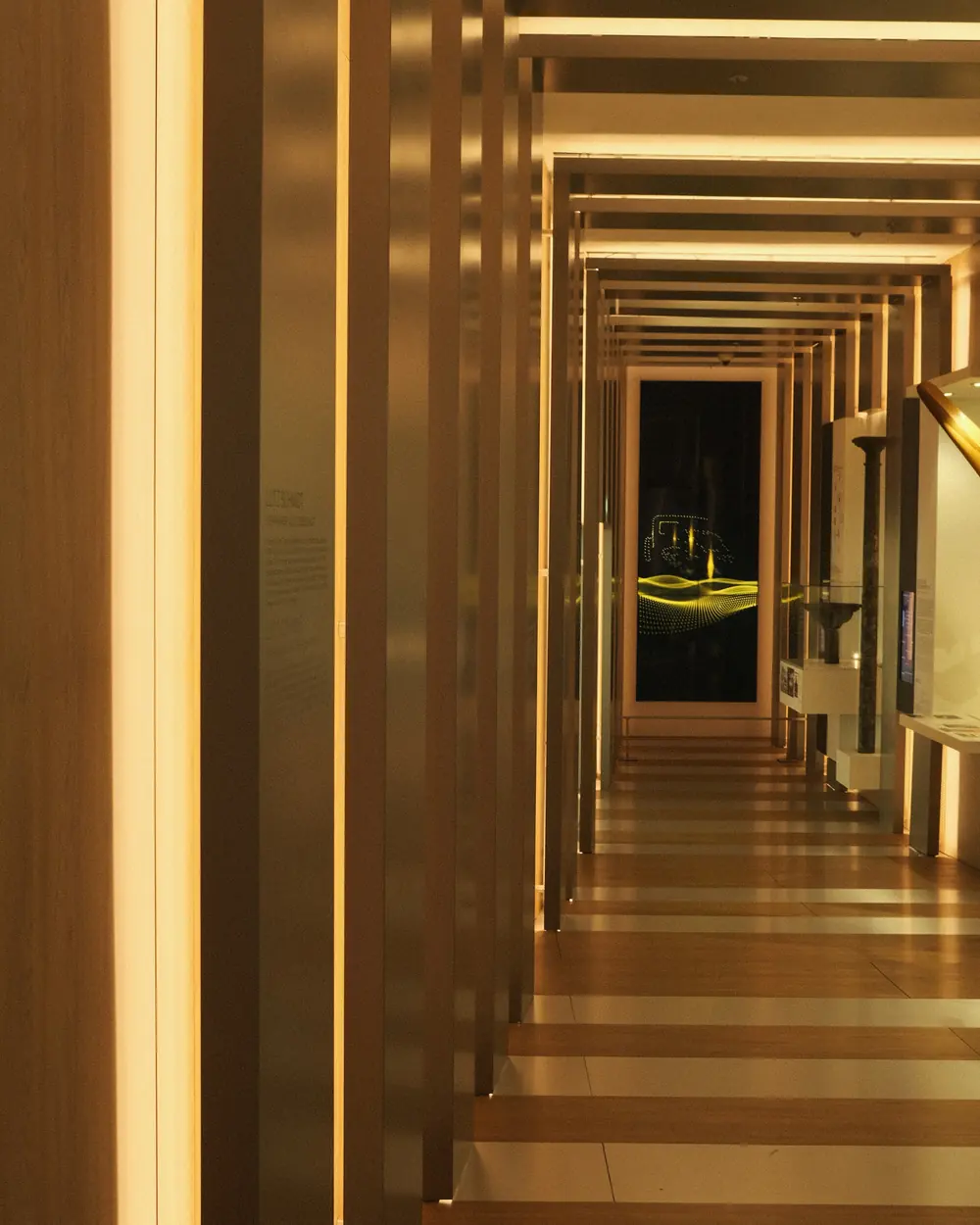 A long corridor of warm timber fins receding toward a lit doorway