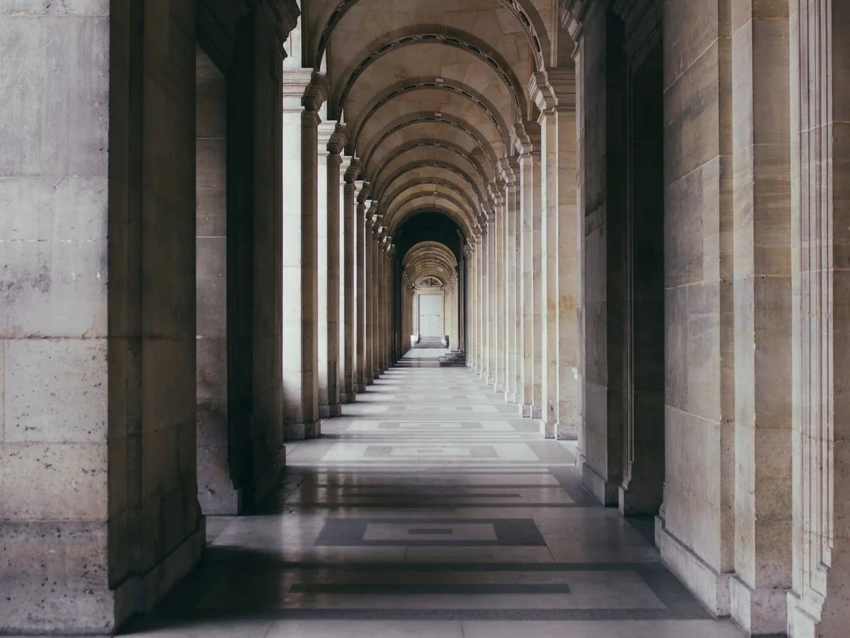 A stone colonnade receding toward a distant doorway, its arches repeating down the corridor