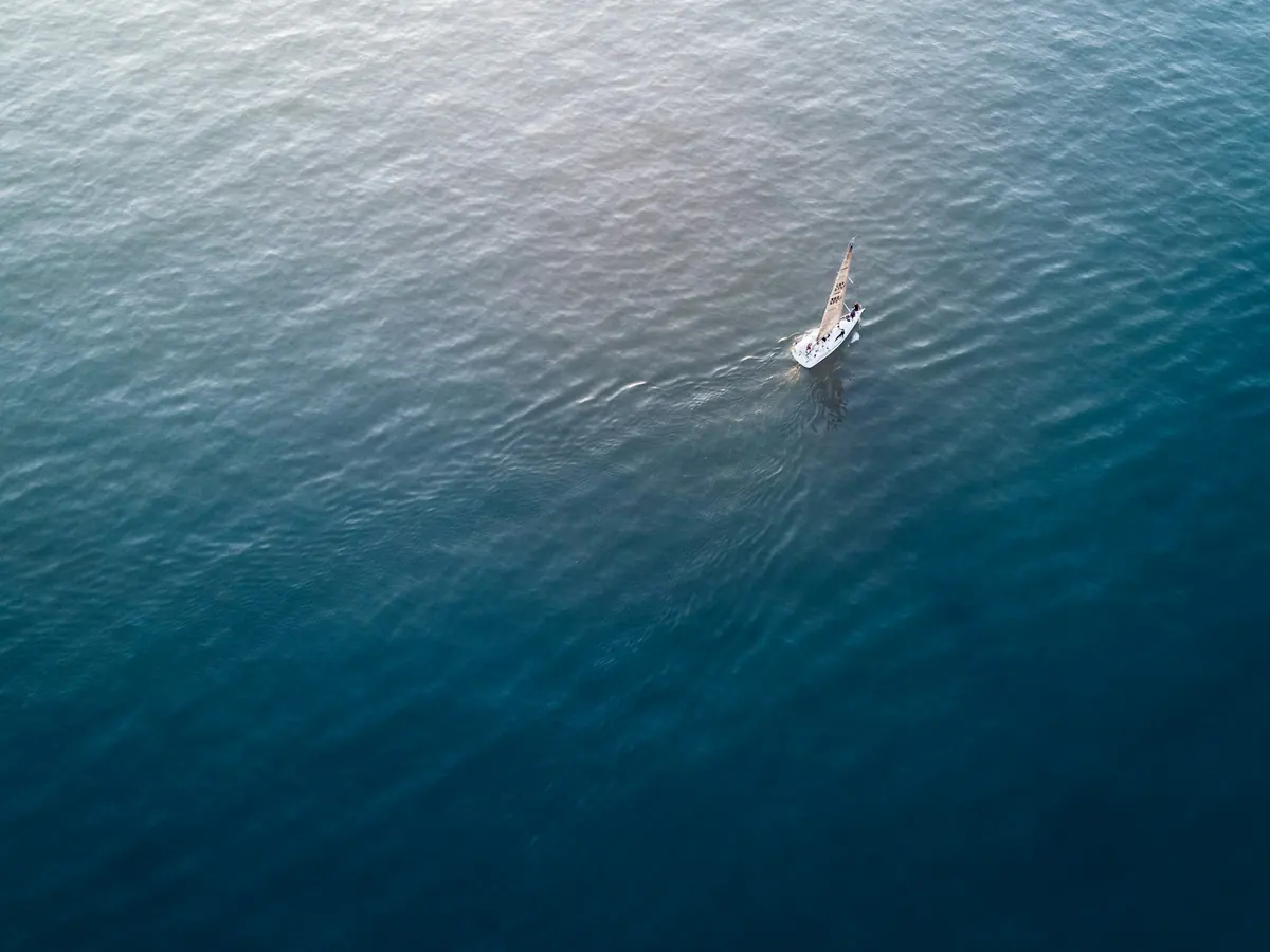 A single small sailboat on a wide expanse of open water, seen from above
