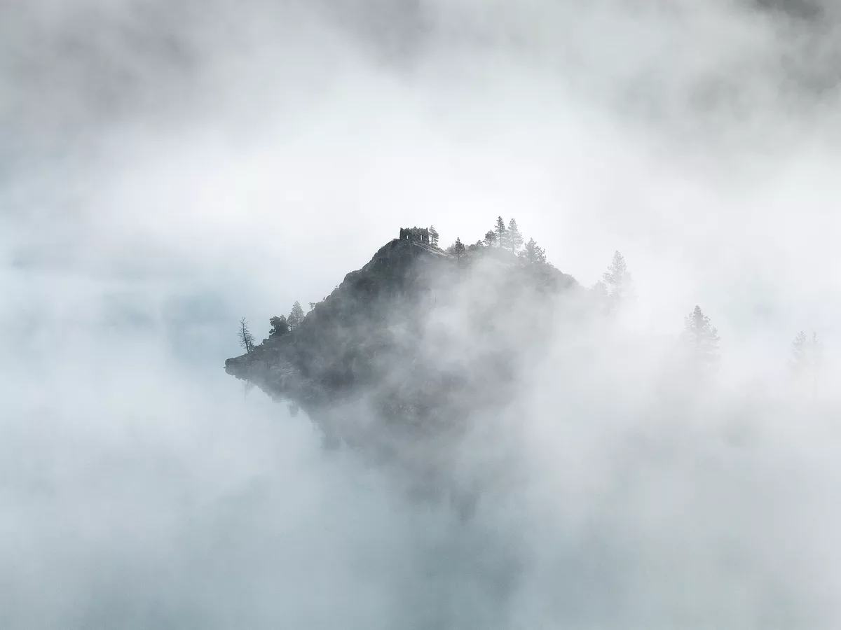 A wooded island emerging from heavy fog, its far side still hidden