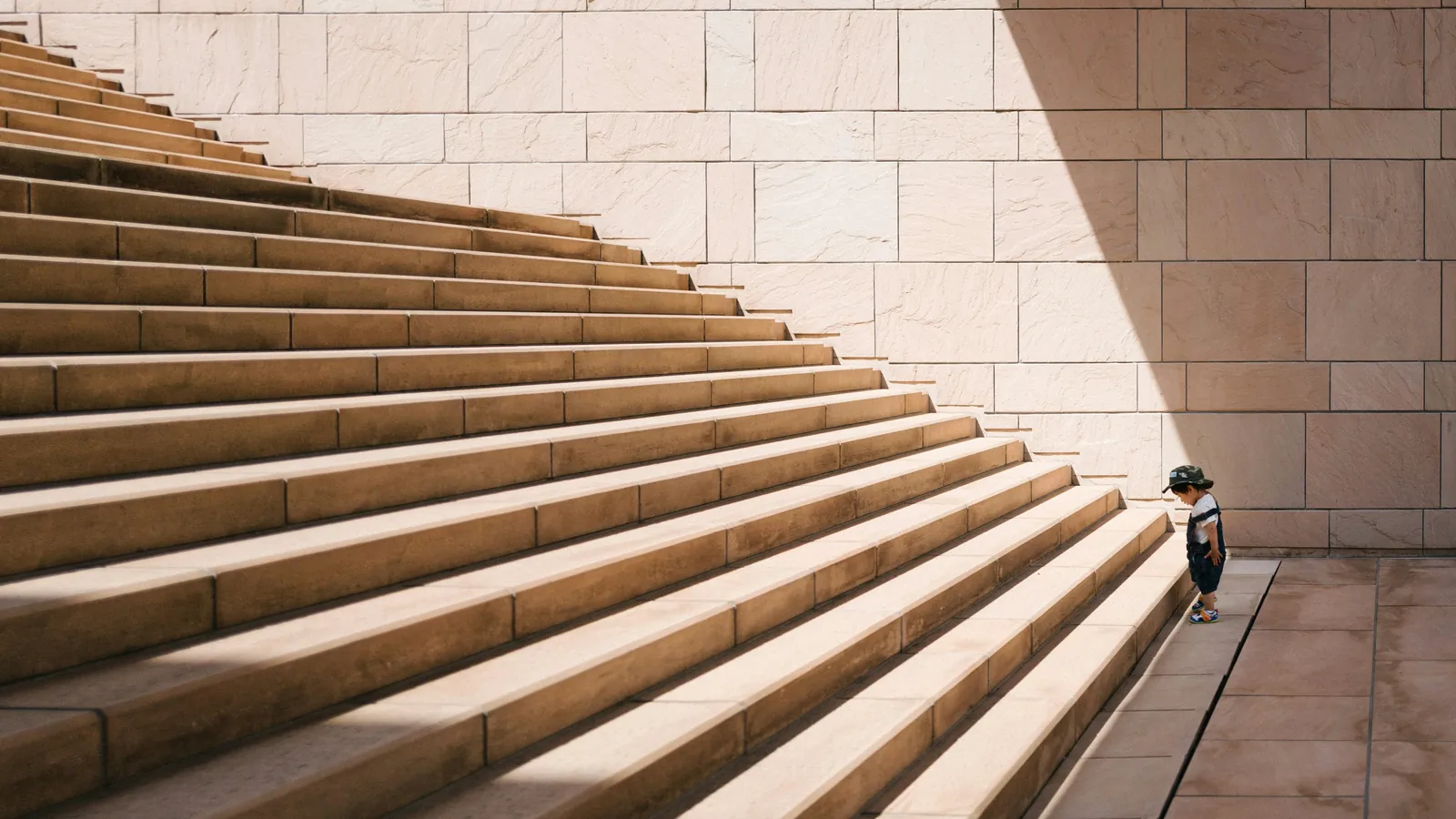 A small child standing at the bottom step of a wide stone staircase