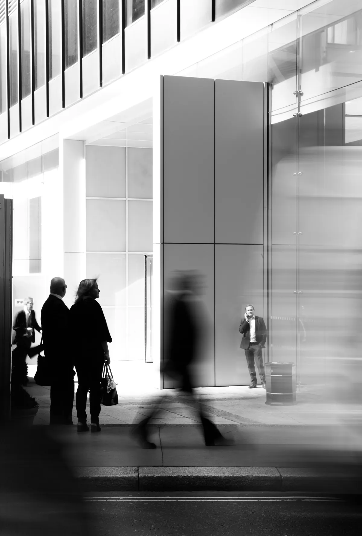 A city sidewalk in monochrome, one figure in sharp focus while others blur past