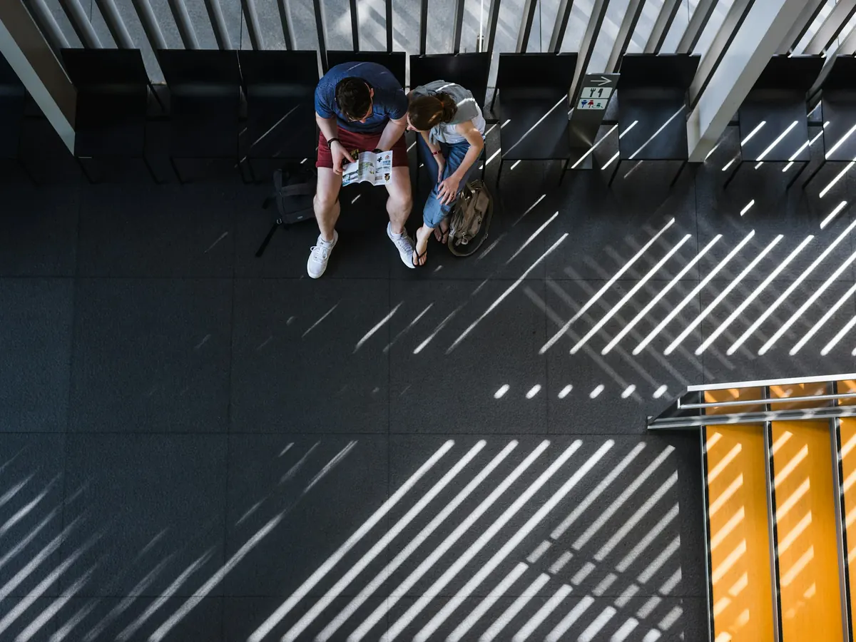 Two people seated together in a large daylit hall, dwarfed by the architecture