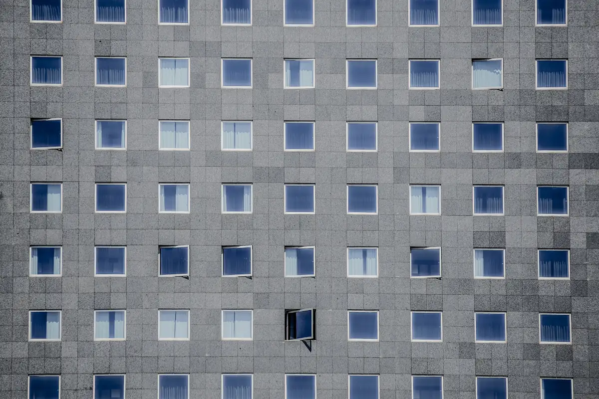A gray facade of identical square windows, one of them standing open
