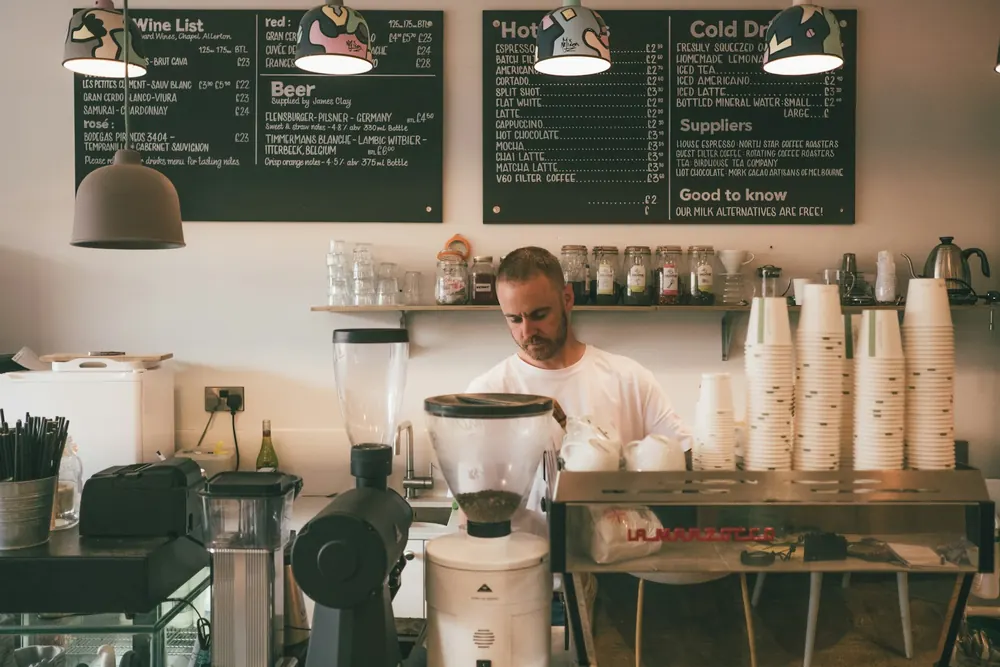 A barista behind a café counter lined with cups